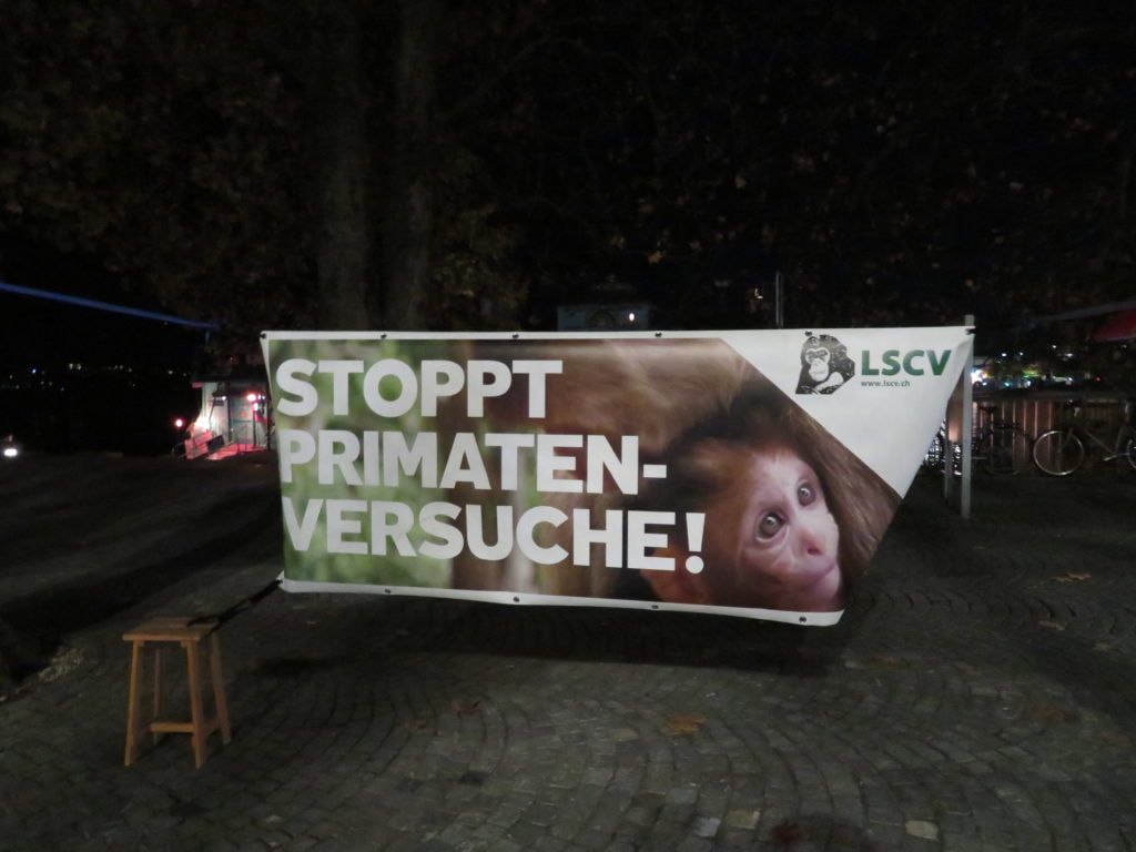 Ein Transparent mit der Aufschrift "Stoppt Primatenversuche" sowie "LSCV" ist zwischen zwei Bäumen aufgehängt..