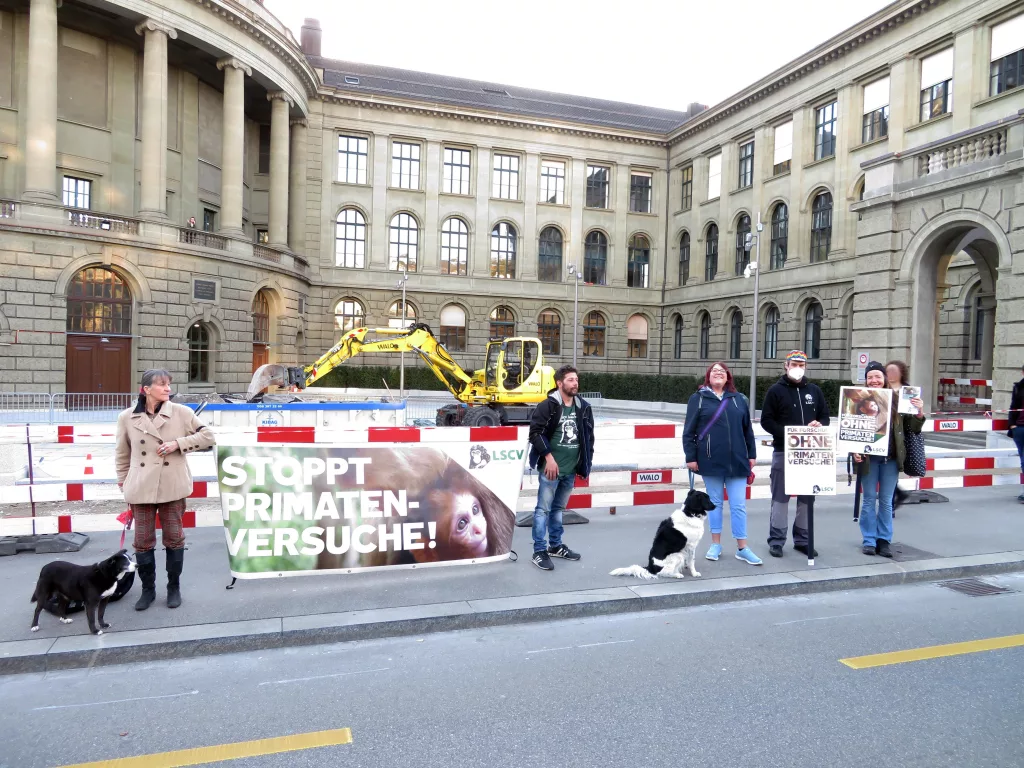 Aktivist*innen stehen mit einem Transparent und Plakten mit der Aufschrift "Stoppt Primatenversuche!" sowie "LSCV“ vor dem Hauptgebäude der ETH. Einzelne Aktivist*innen tragen eine Mund-Nasenbedeckung.