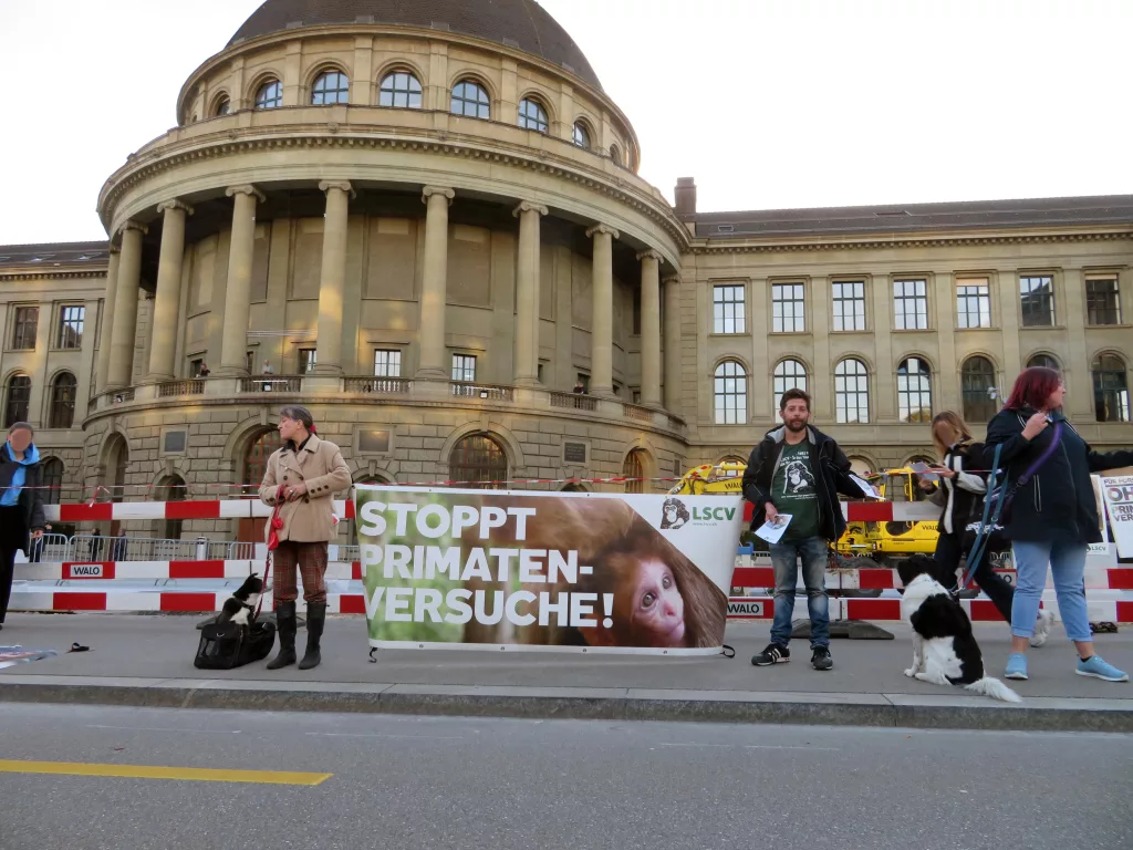 Aktivist*innen stehen mit einem Transparent und Plakten mit der Aufschrift "Stoppt Primatenversuche!" sowie "LSCV“ vor dem Hauptgebäude der ETH.